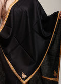 Black shawl with gold embroidery draped over a person, against a neutral background