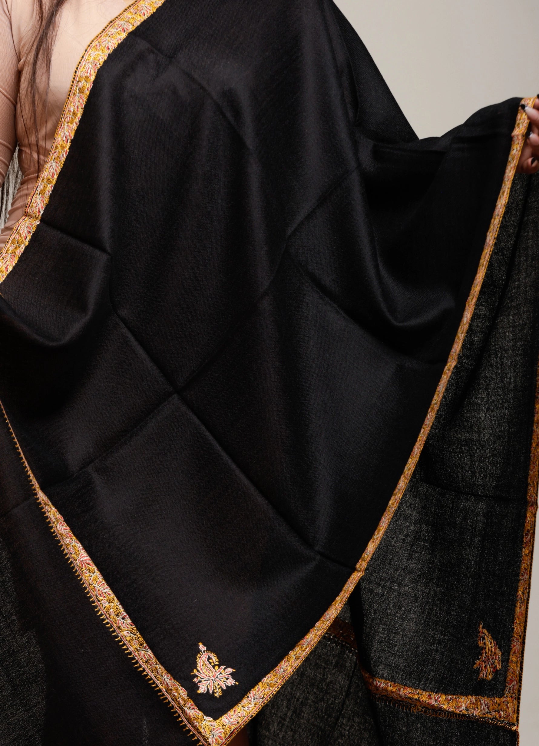 Black shawl with gold embroidery draped over a person, against a neutral background