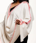 White shawl with red embroidery draped over a person on a white background