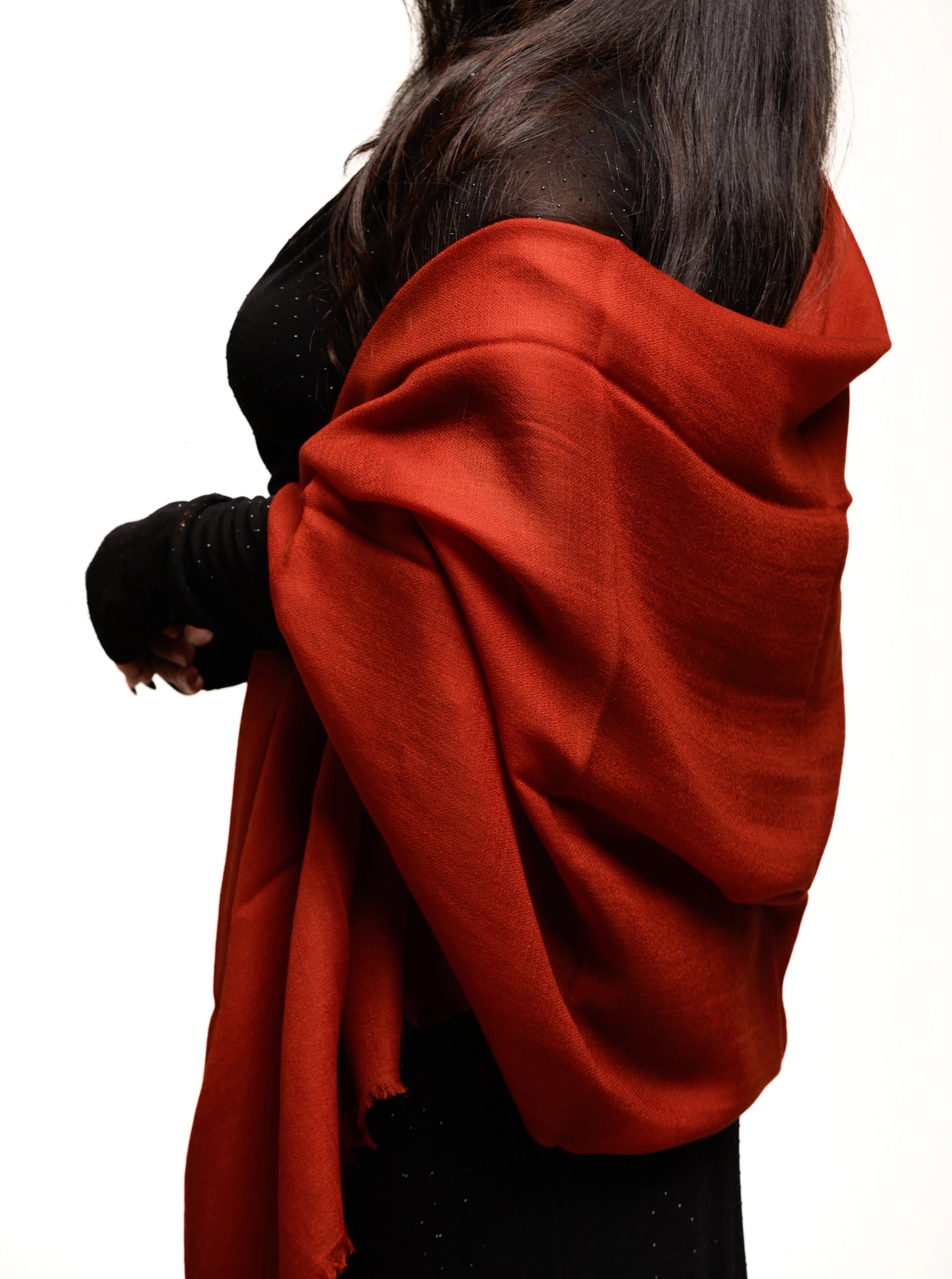 A person wearing a bright rust-red shawl or wrap draped over the shoulders, paired with a black top and black gloves, shown against a plain white background.