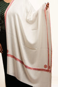 White shawl with red embroidered border held by a person on a white background