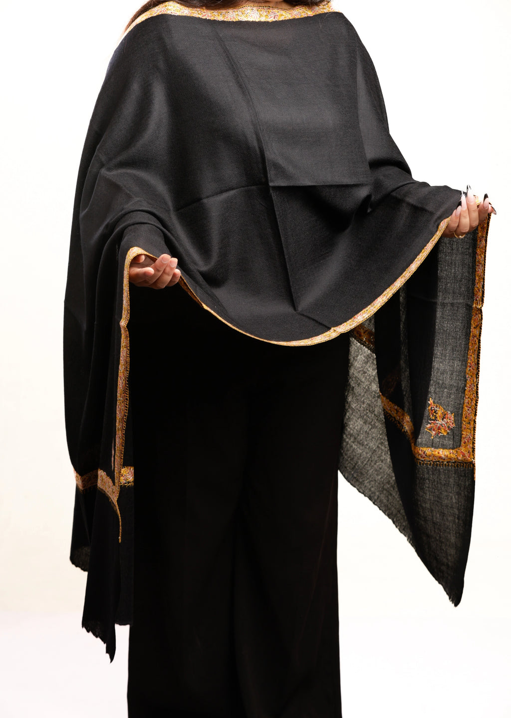 Black shawl with gold trim held by a person on a white background