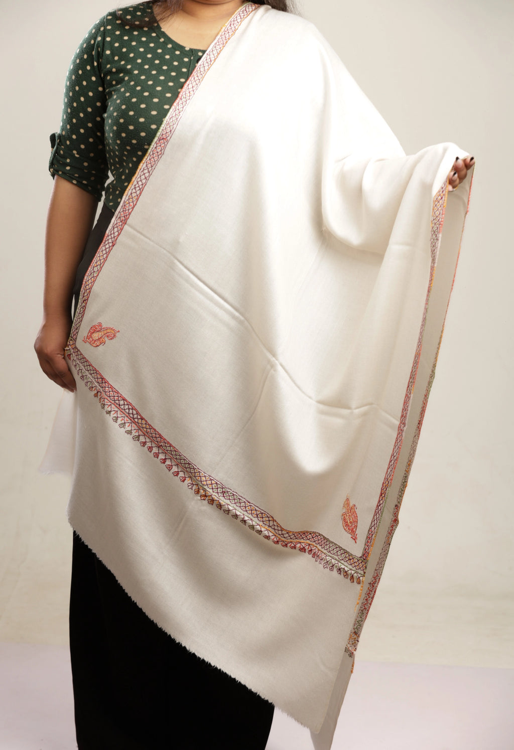 Person wearing a white scarf with red embroidery on a plain background