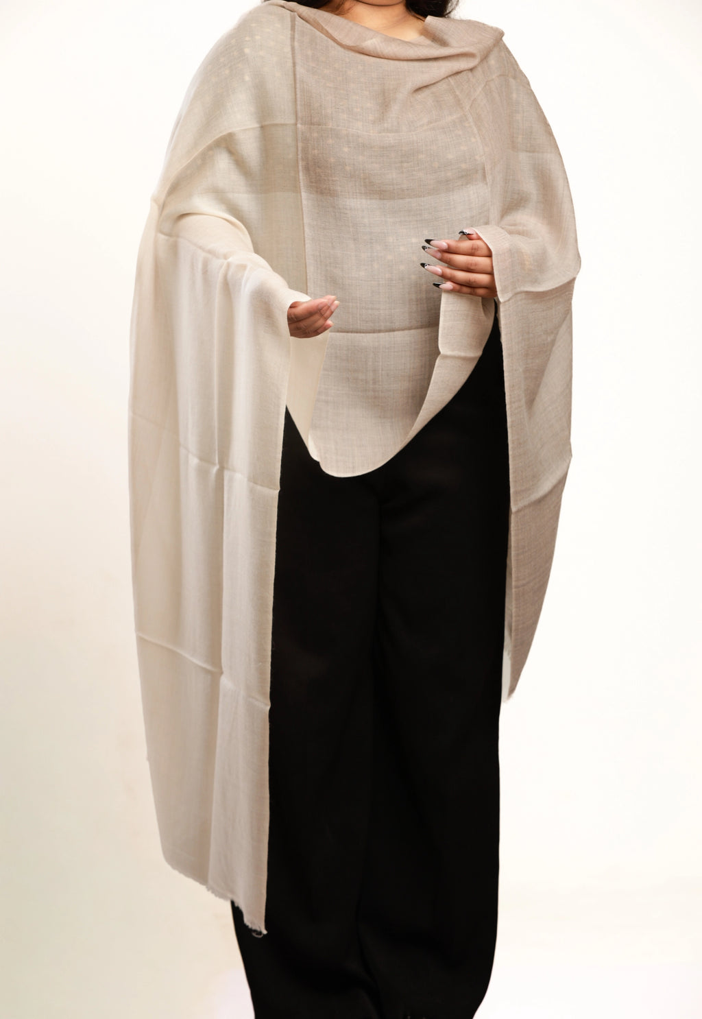 Person wearing a beige poncho over a black outfit on a white background