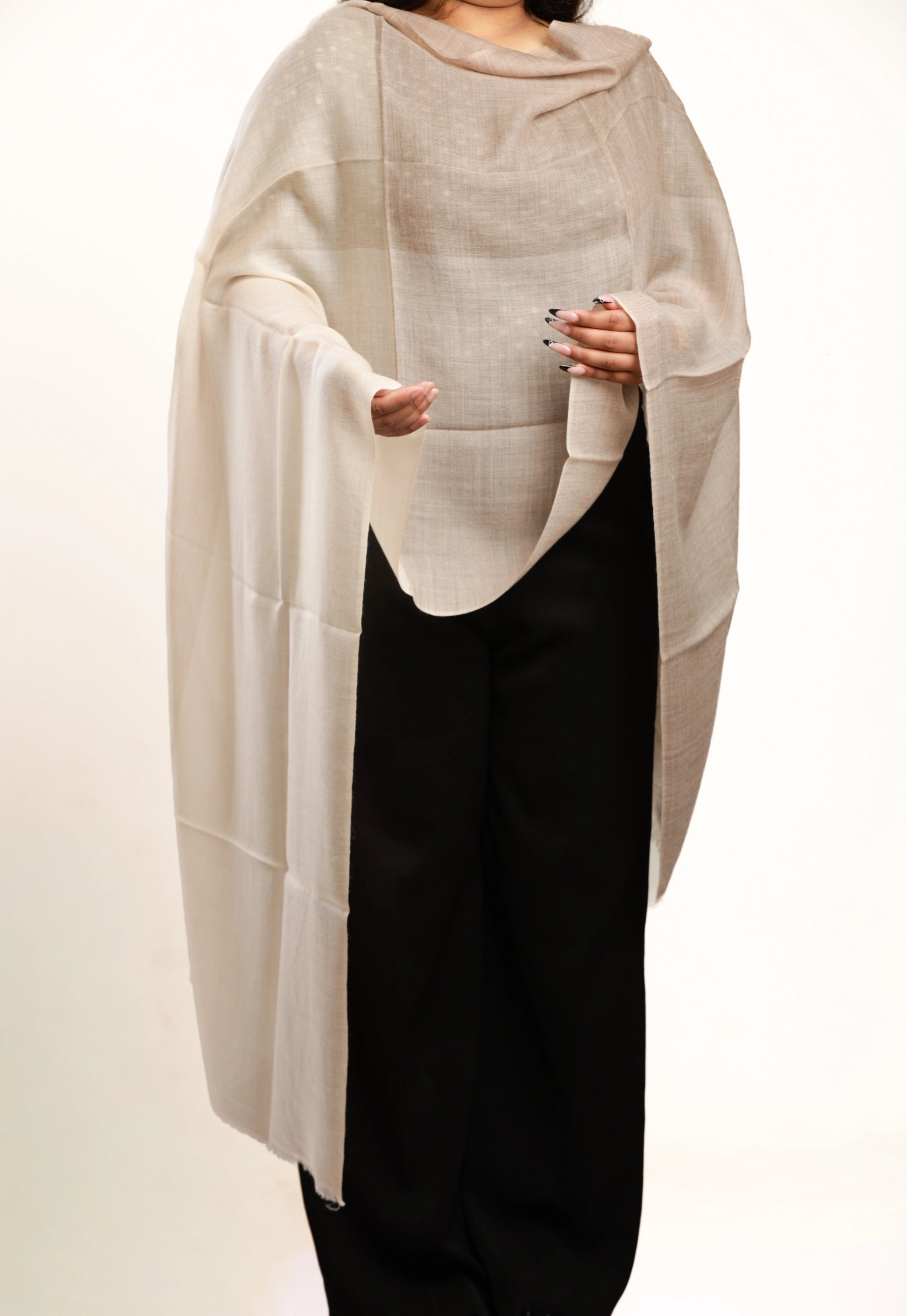 Person wearing a beige poncho over a black outfit on a white background