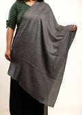 Person wearing a gray shawl over a green and black patterned top on a beige background