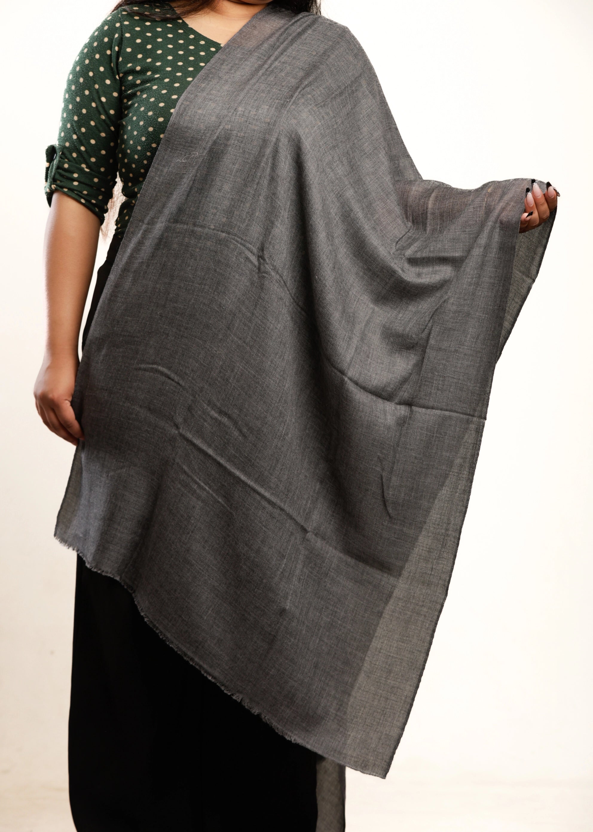 Person wearing a gray shawl over a green and black patterned top on a beige background