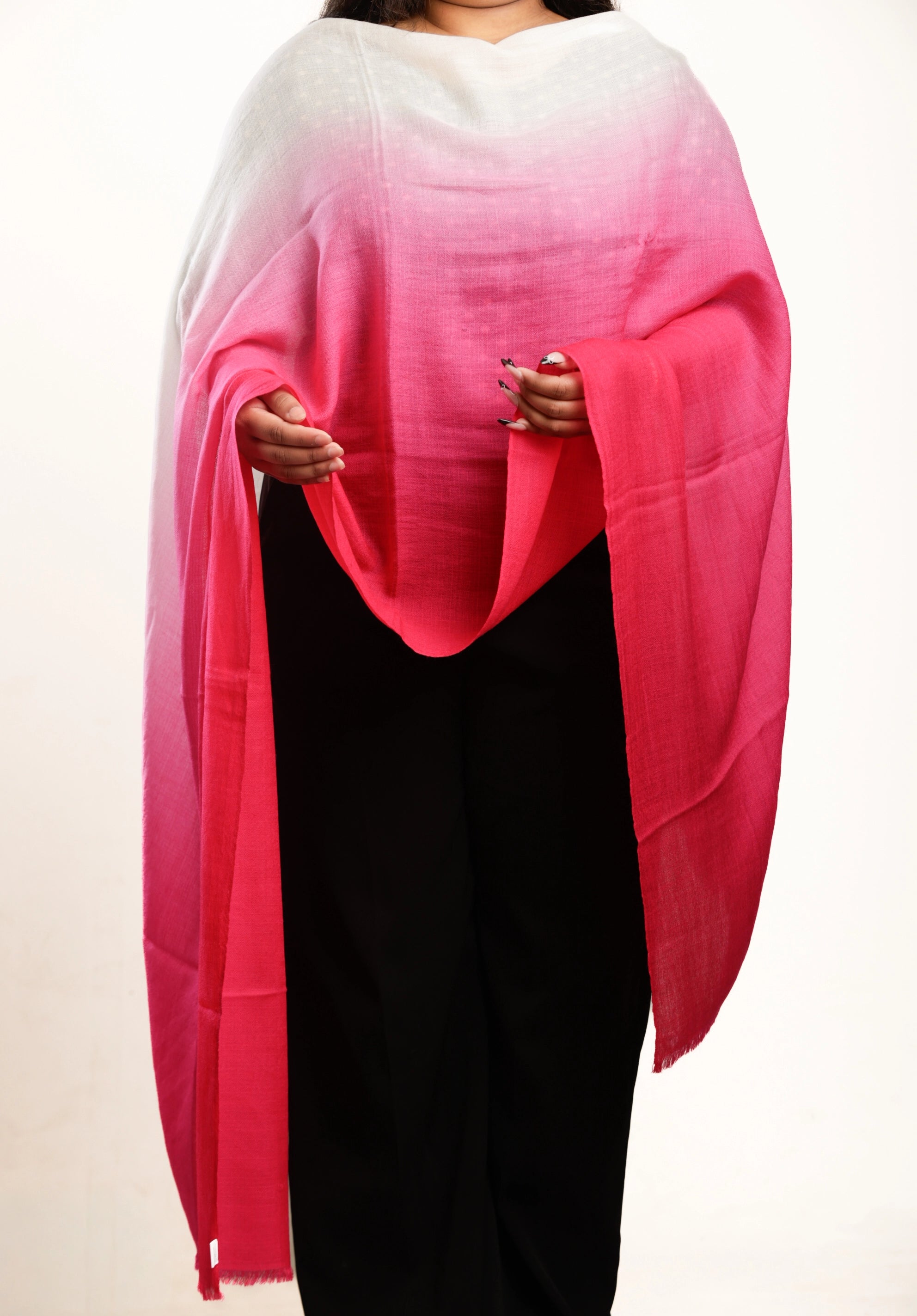 A person wearing a lightweight shawl with a white-to-pink-to-coral ombré gradient, paired with black pants, against a plain white background.