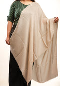 Person wearing a beige shawl over a green and black patterned top on a white background