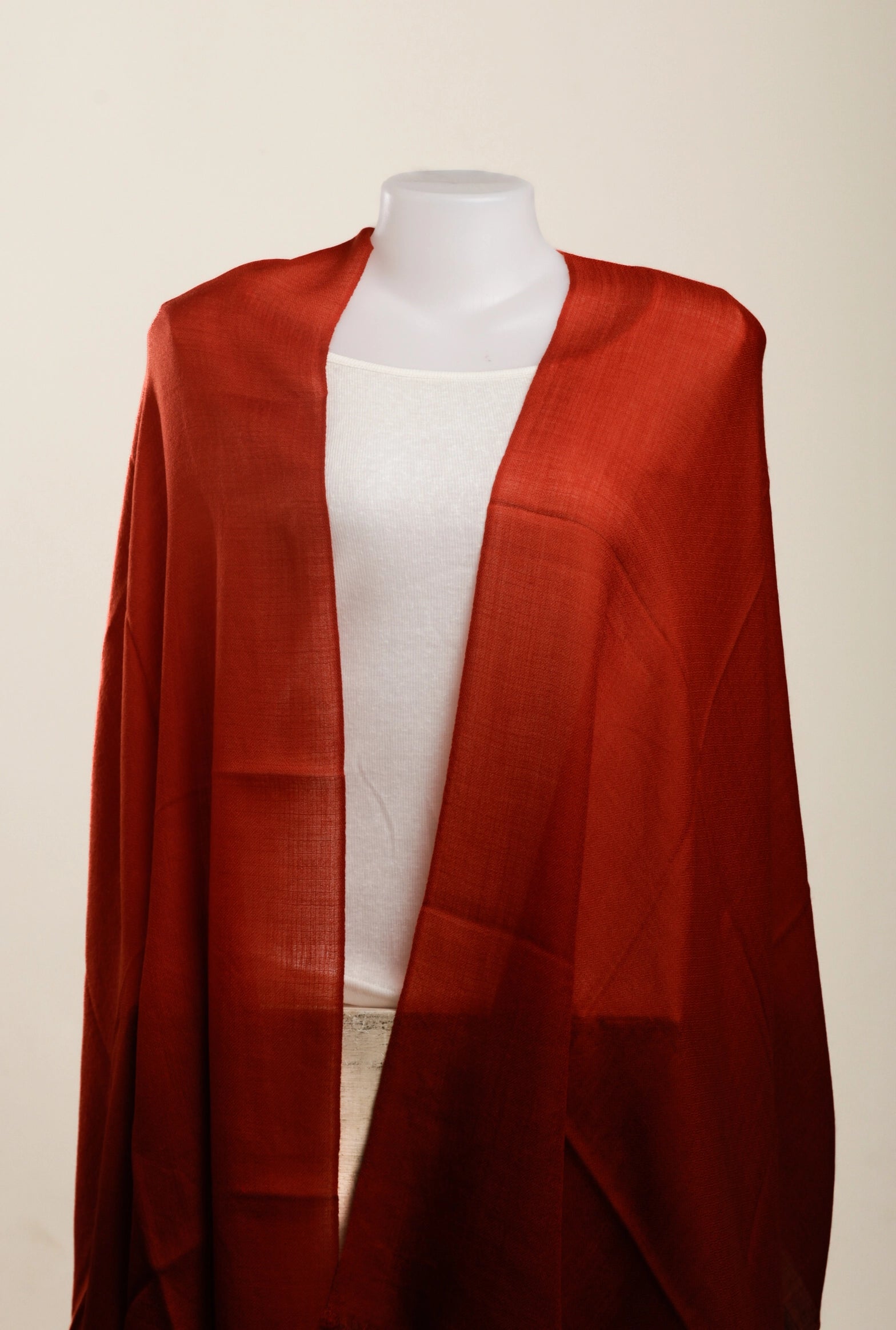 A rust-red open-front shawl or lightweight wrap draped over a white mannequin torso against a plain light beige background.