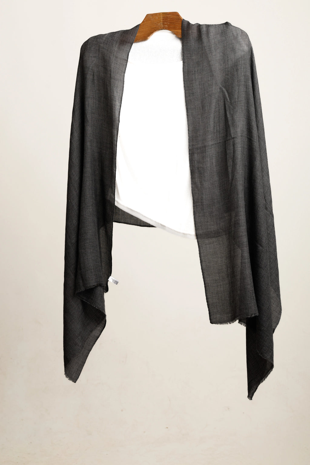 Gray shawl on a wooden hanger layered over a white top against a white background