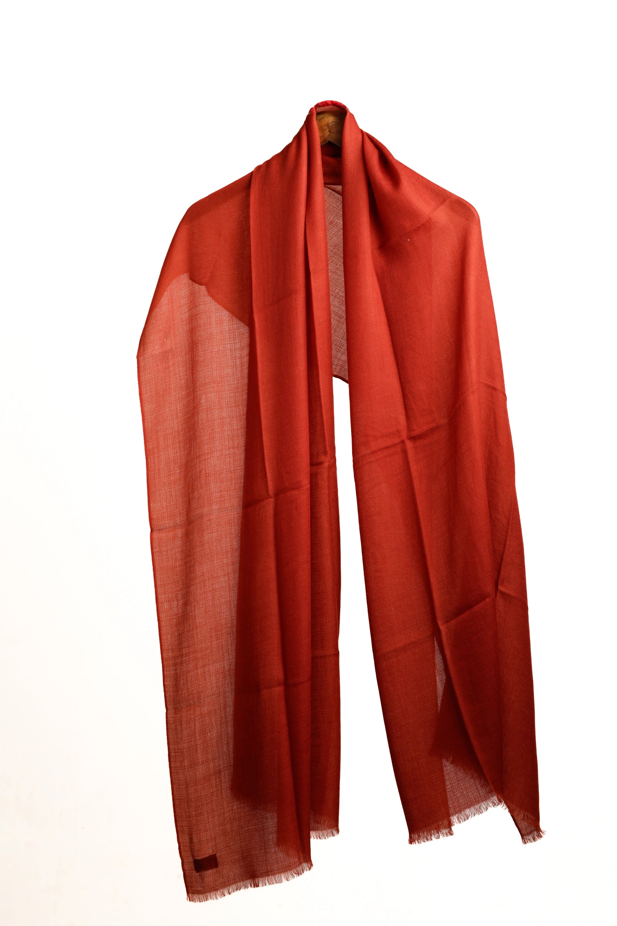 A vibrant rust-red or burnt orange scarf draped elegantly on a hanger against a plain white background.