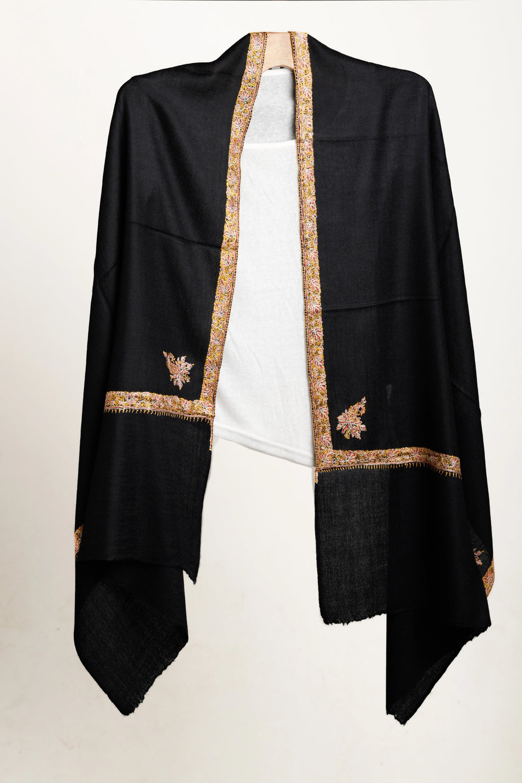 Black shawl with gold embroidery layered over white top on a white background