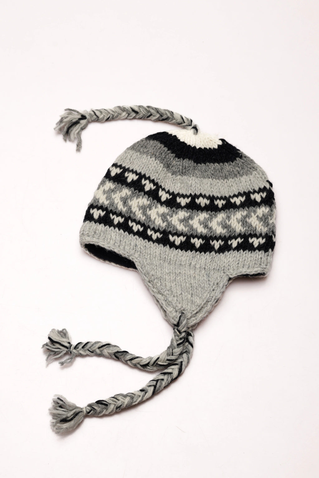 Knitted grey and black hat with braided earflaps on a white background