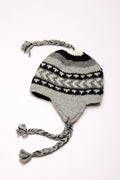 Knitted grey and black hat with braided earflaps on a white background