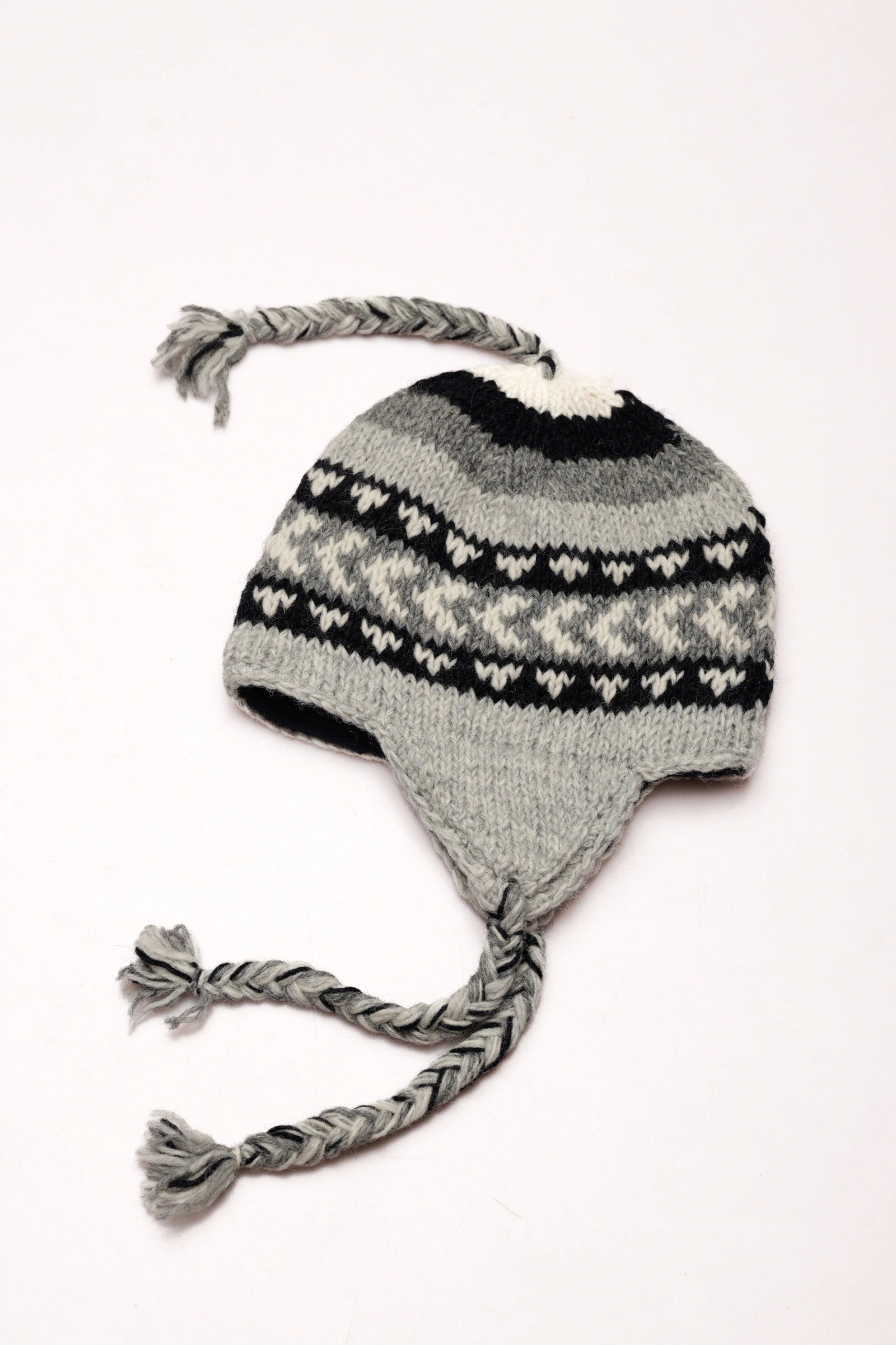 Knitted grey and black hat with braided earflaps on a white background