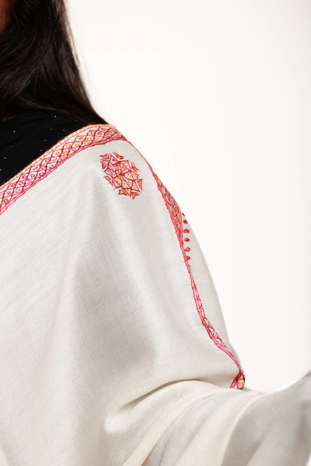 Close-up of a white garment with red embroidery on a plain background