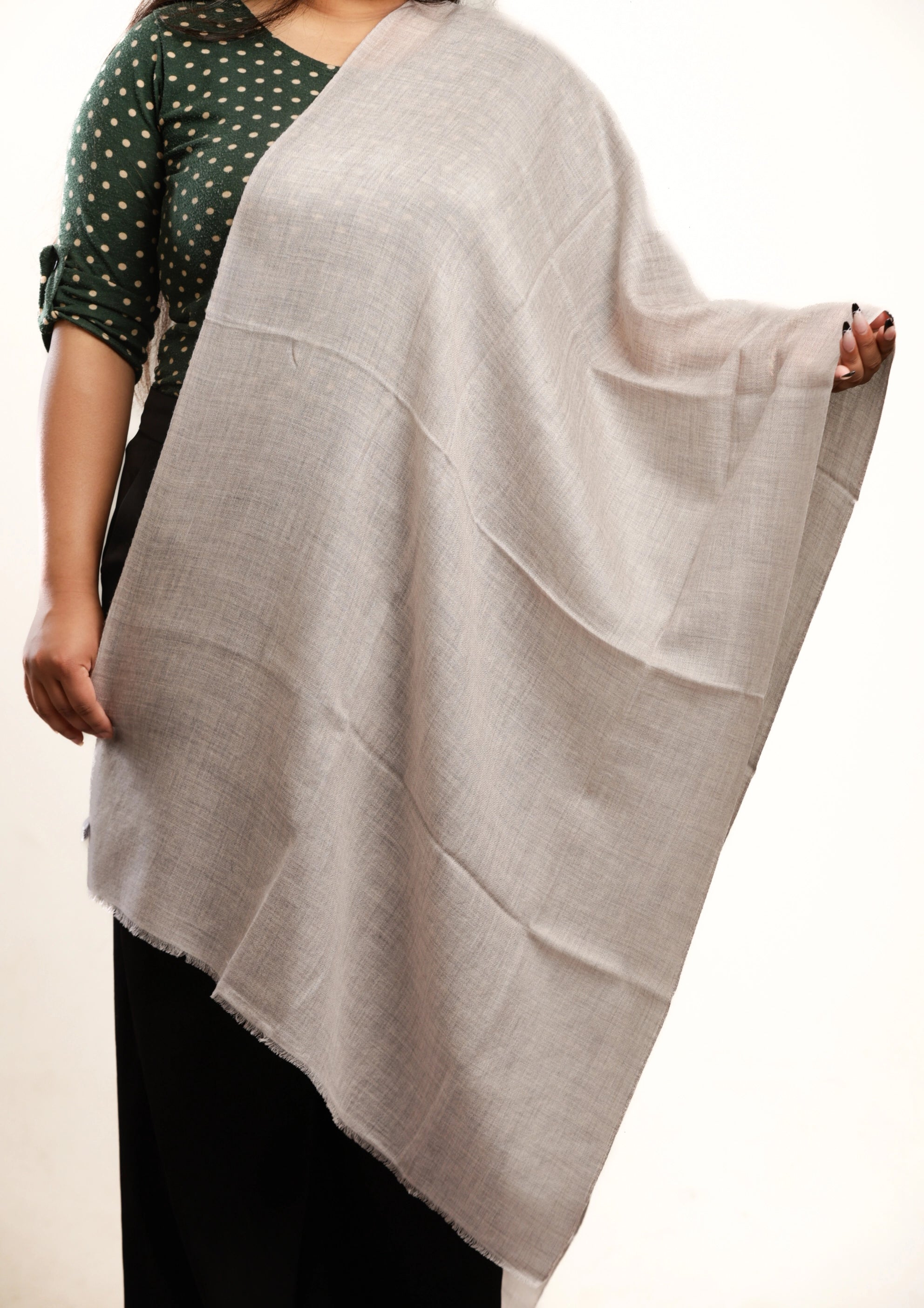 Person wearing a light gray shawl over a green and black patterned top on a white background