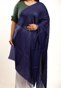 Person wearing a blue shawl over a green and white polka dot top on a beige background