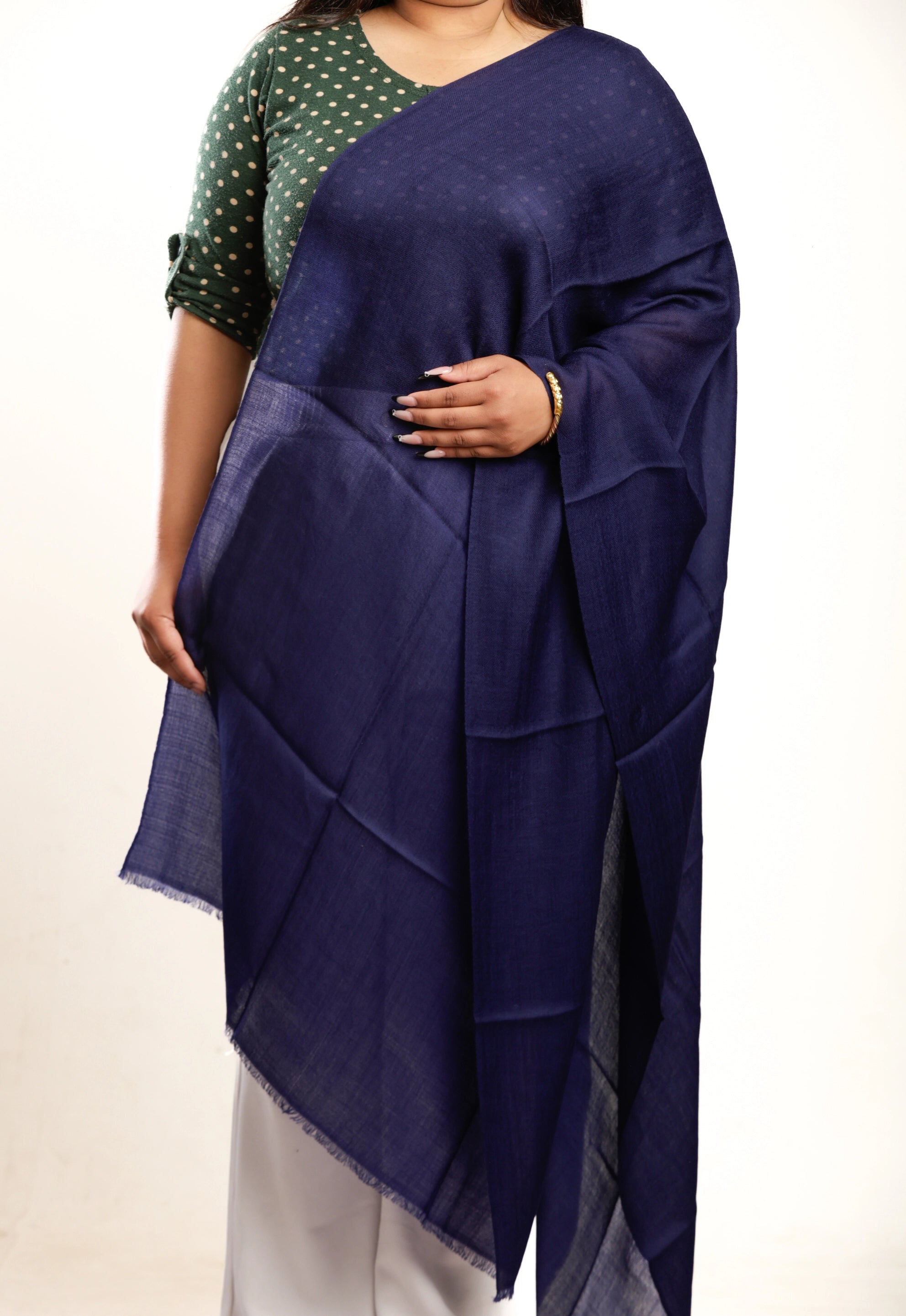 Person wearing a blue shawl over a green and white polka dot top on a beige background