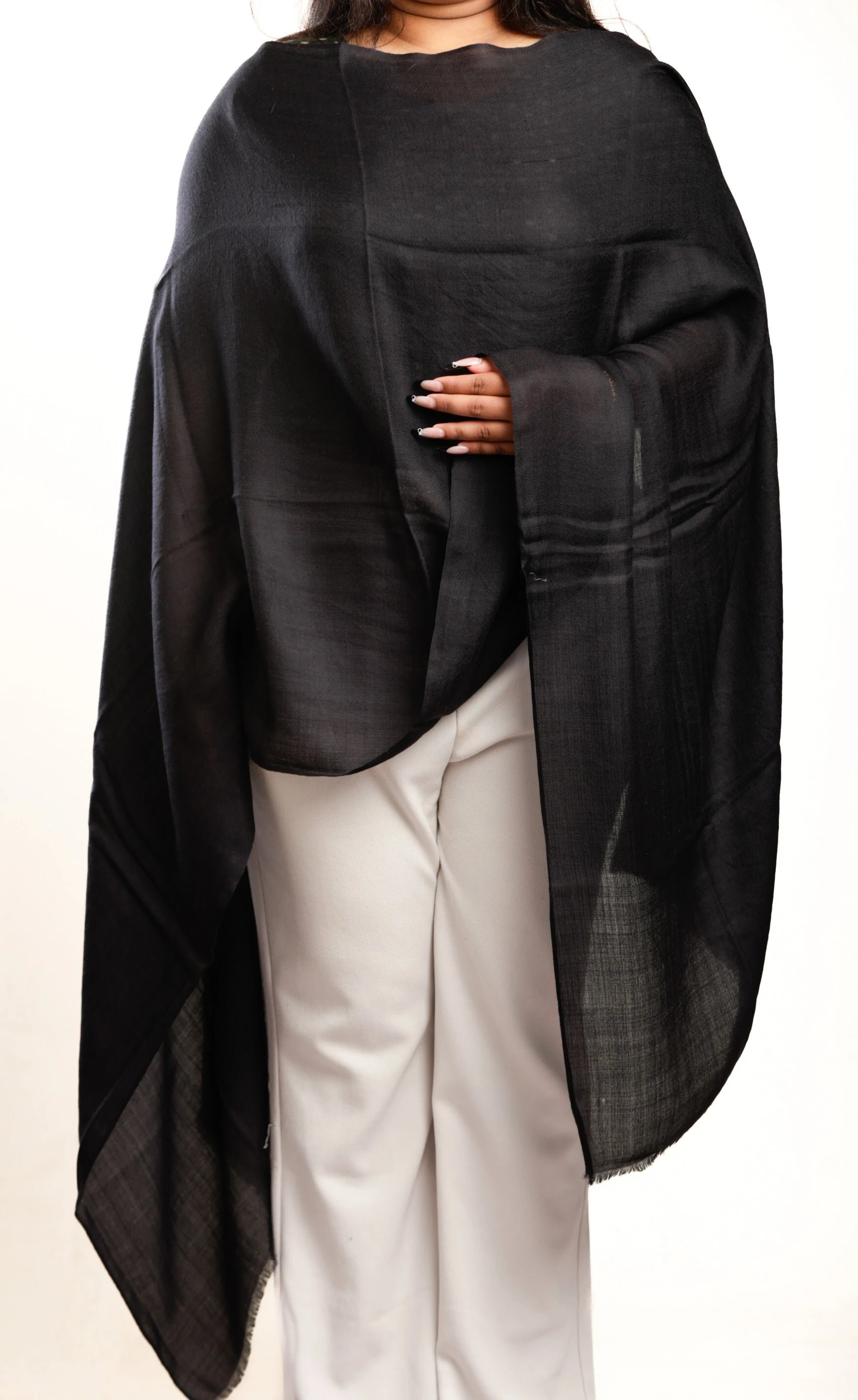 Person wearing a black shawl over a plain background