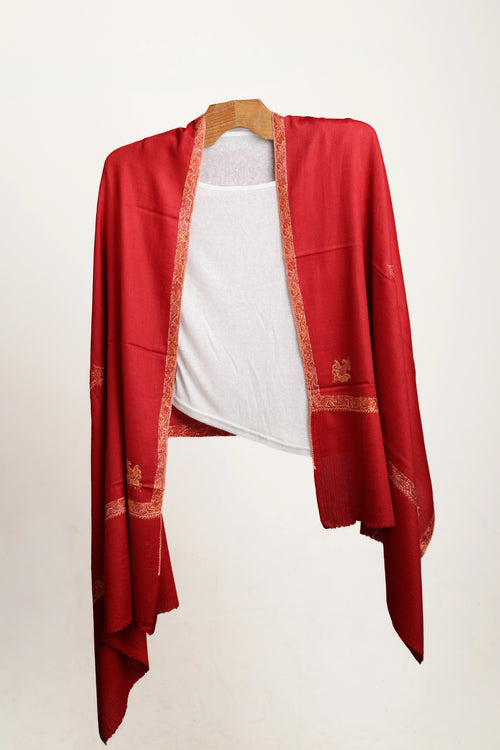 Red shawl with gold embroidery layered over white top over a wooden hanger on a white background