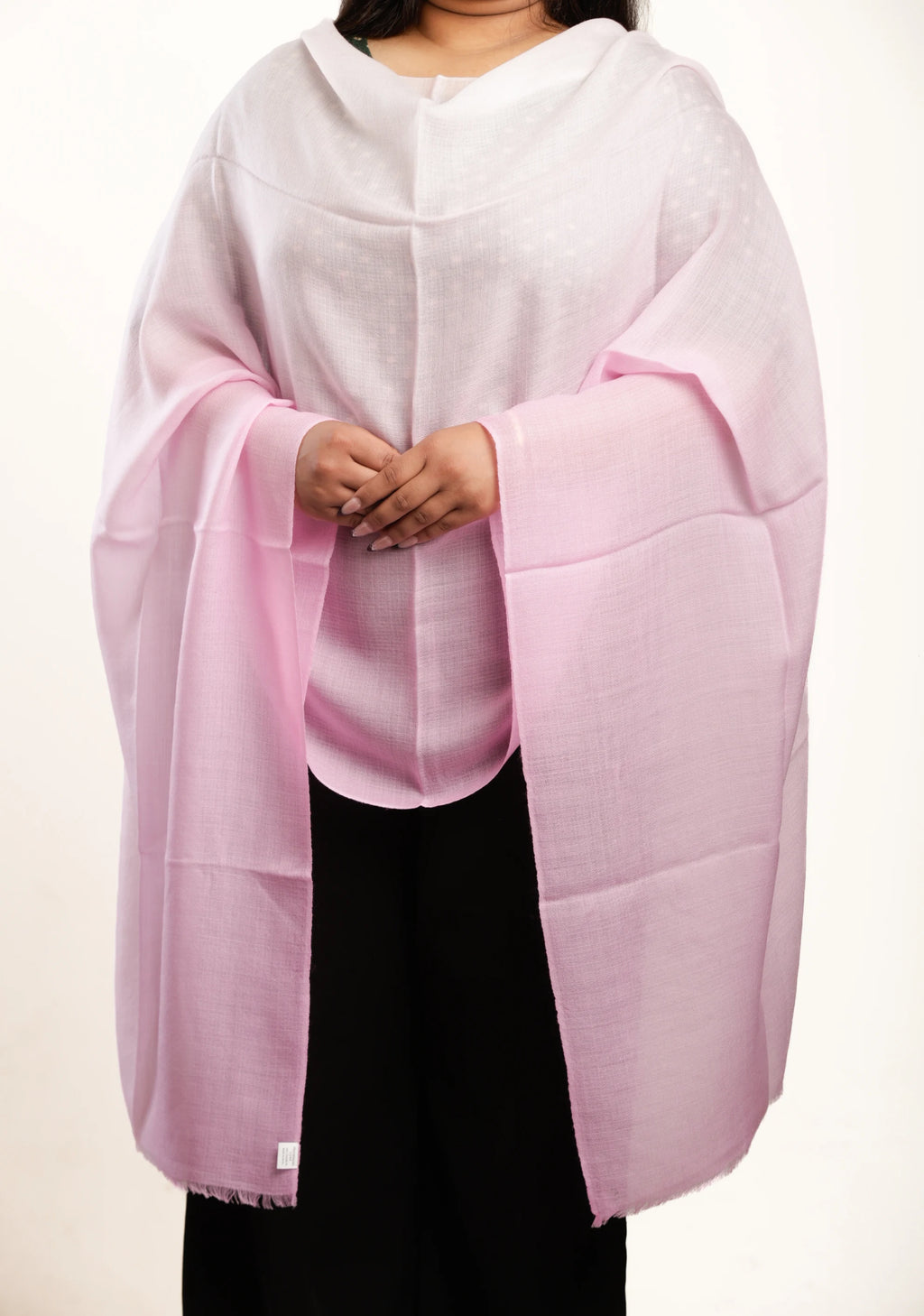 A person wearing a light pink shawl or wrap over a white top and black pants, photographed against a plain light background.
