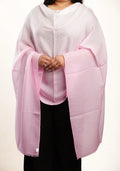 A person wearing a light pink shawl or wrap over a white top and black pants, photographed against a plain light background.
