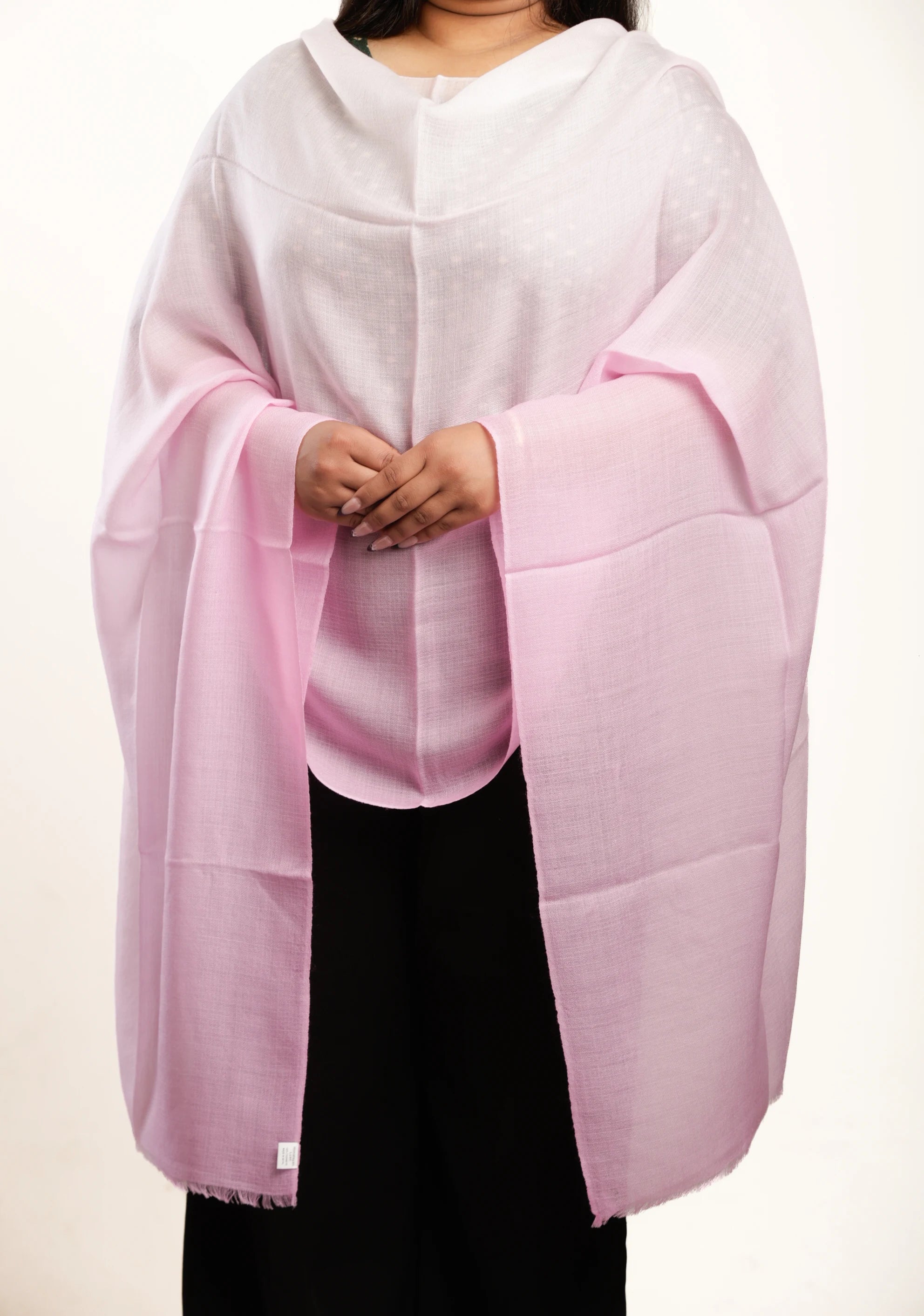 A person wearing a light pink shawl or wrap over a white top and black pants, photographed against a plain light background.